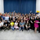 Dezenas de pessoas posam para uma foto, muitas seguram um papel na mão