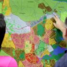 Homem de costas e camisa mostra mapa de Joinville para mulher ao lado dele, de costas, de blusa rosa