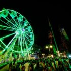 Roda gigante iluminada em praça com muitas visitantes