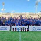 Atletas em campo de futebol posam para foto com medalhas penduradas nos pescoços
