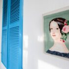 Quadro em parede feito de tapeçaria tem imagem de uma mulher com cabelo preso com flores