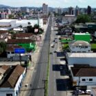 Imagem aérea de rua com quatro pistas para carros, além de comércios e casas