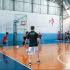 Meninos jogam basquete em quadra, com técnico supervisionando