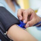 Profissional de saúde usa estetoscópio em braço de paciente que também tem medidor de pressão