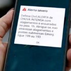 Pessoa segura celular na mão, na tela do aparelho está escrito um alerta da Defesa Civil
