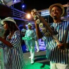Homem e mulher com fantasia de Carnaval tocam instrumentos de percussão na avenida