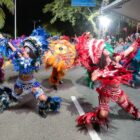 Pessoas com fantasias de Carnaval desfilam em avenida perto de palanque