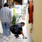 Mulher agachada com colete coloca tela em ralo enquanto outra mulher em pé observa.