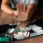 Homem faz gesto com a mão rejeitando comprimidos, drogas e seringa em cima de uma mesa