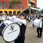 Alunos de fanfarra desfilam e tocam em avenida uniformizados e com instrumentos musicais
