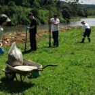 Pessoas em área verde perto de rio com pás e enxadas