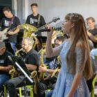 Menina canta com microfone na mão, músicas tocam ao lado dela