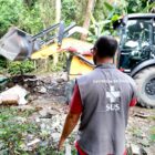 Homem com colete do SUS observa máquina escavadeira realizar limpeza em área