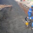Dois homens com uniformes e capacetes trabalham em obra com equipamentos
