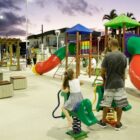 Área pública com playground para crianças, mesas e cadeiras e pessoas utilizando o local