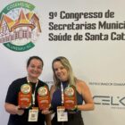 Uma mulher morena e uma loira seguram troféus