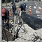 Homens com uniforme e capacete trabalham em rede de esgoto