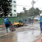 Homens com capacetes trabalham em obra em rua com equipamentos
