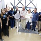 Pessoas com medalhas no pescoço posam para foto, algumas seguram um selo de reconhecimento
