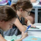 Duas meninas sentadas escrevem em cadernos em carteiras