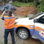 Homem de colete laranja da Defesa Civil fotografa área com terra que cedeu após chuva