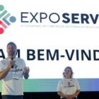 Prefeito e vice prefeita em palco, ele segura um microfone