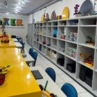 Laboratório de criatividade, sala com estantes cinzas, mesas amarelas e cadeiras azuis