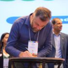 Secretário com camisa azul escura e crachá assina documento
