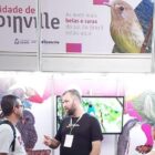 Stand de Joinville com imagens de pássaros, pessoas conversam em frente