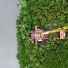 Imagem aérea de construção de ponte, com equipamentos como guindaste em margem do rio