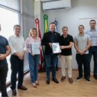 Seis homens e uma mulher posam para foto, dois seguram um relatório