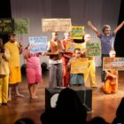 Pessoas seguram cartazes sobre saúde mental em palco em peça de teatro