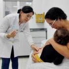 Mãe segura criança no colo enquanto profissional de saúde prepara para aplicar vacina