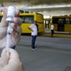 Profissional de saúde manipula seringa e frasco de vacina em terminal de ônibus