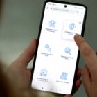 Mulher segura celular e na tela está o portal de serviços da Prefeitura de Joinville