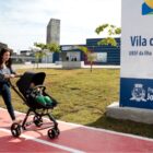 Mulher empurra carrinho de bebê e caminha ao lado de outra criança em nova Vila da Saúde