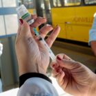 Mulher manuseia seringa e frasco com vacina em terminal de ônibus