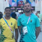Dois atletas, um moreno com camiseta amarela e outro loiro com camiseta azul, posam para foto