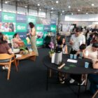 Stand em feira de imóveis, pessoas sentadas sendo atendidas e outras a espera