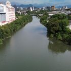 Foto do rio Cachoeira, com vegetação nas margens e um moinho perto