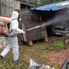 Homem com roupa especial aciona fumacê em área com lixo