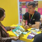 Homem conversa com duas mulheres em stand de turismo em feira
