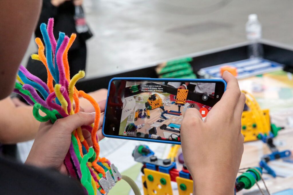 Mãos de criança seguram celular e peças usadas em robô