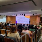 Auditório com pessoas sentadas enquanto uma pessoa faz apresentação