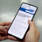 Mão segura celular com processo de inscrição da Escola Agrícola