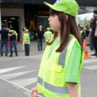 Menina com uniforme verde segura placa de pare diante da faixa de pedestres