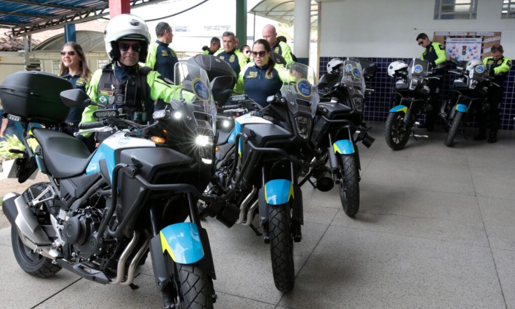 Novas motocicletas do Detrans alinhadas e agente de trânsito com capacete diante de uma delas