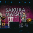 Homem e mulher com roupas e instrumentos orientais se apresentam em palco durante o Sakura Joinville