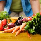 Homem segura caixa de madeira com legumes e verduras