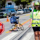 Menina com colete e boné refletivos segura placa de pare perto de faixa de pedestres